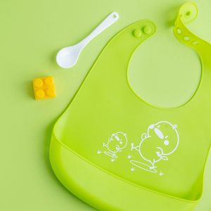 Baby porridge with cutlery on green background. Baby food concept.